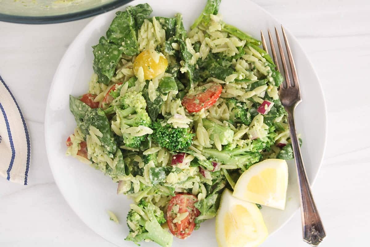 A small plate with a serving of pesto orzo pasta salad with broccoli and tomatoes.